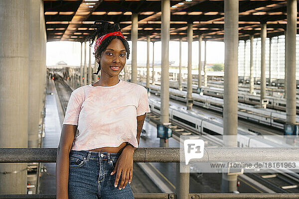 Smiling young woman leaning on railing at railroad station