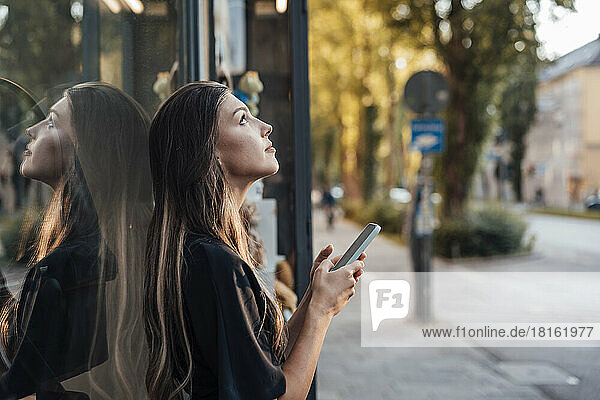 Young woman with mobile phone standing by glass wall