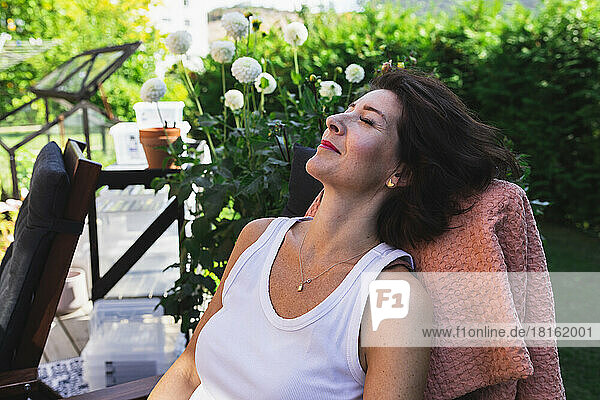 Lächelnde Frau mit geschlossenen Augen ruht auf einem Stuhl auf der Terrasse