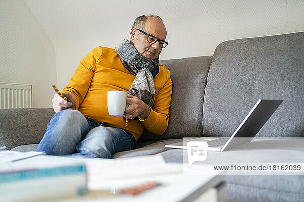 Man holding cup watching laptop on sofa at home