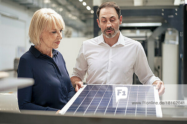 Businessman holding solar panel discussing with senior businesswoman in industry