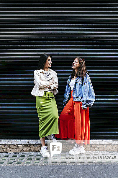 Happy lesbian friends talking to each other in front of shutter