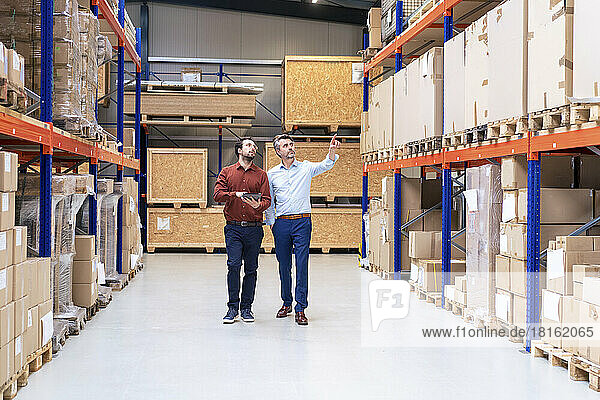 Businessman with colleague pointing at containers in warehouse