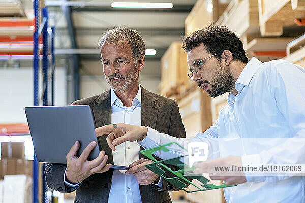Senior businessman with colleague discussing over laptop at warehouse