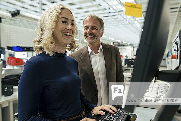Happy businesswoman using computer standing by colleague at industry