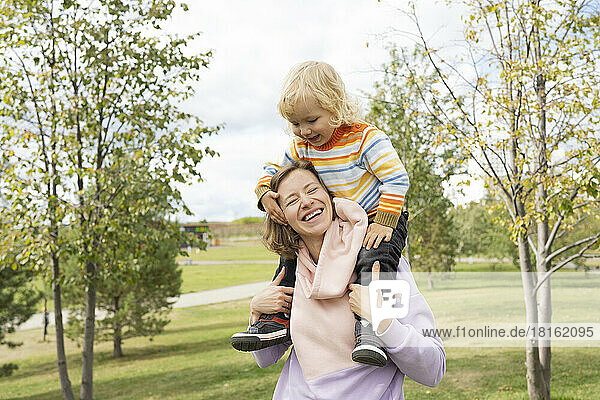 Glückliche Mutter trägt Sohn auf Schultern im Park