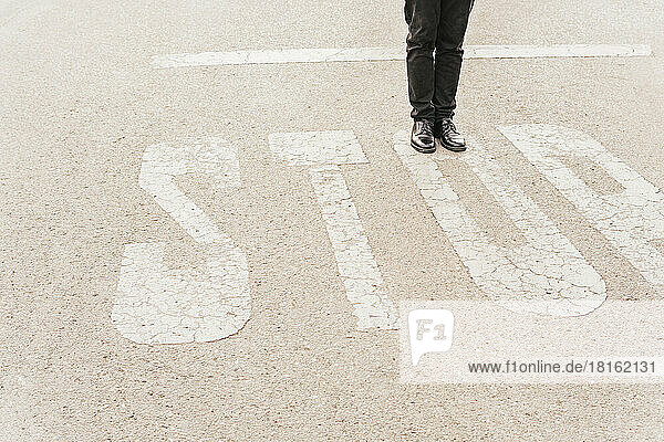 Beine eines Mannes auf einem STOP-Schild an der Straße