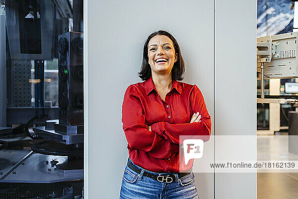 Happy businesswoman with arms crossed standing near column at factory