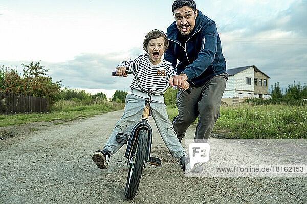 Vater bringt Sohn bei  auf der Straße Fahrrad zu fahren