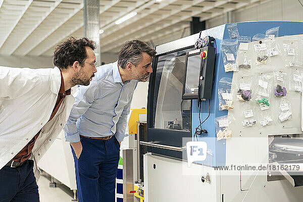 Mature businessman with colleague examining machinery at factory