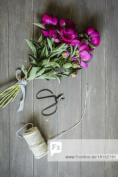 Scissors  string and freshly cut peonies lying on wooden surface