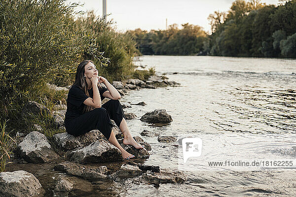 Woman with hands on chin sitting by lake