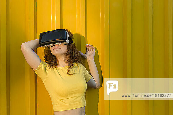Smiling woman wearing virtual reality simulator in front of yellow wall