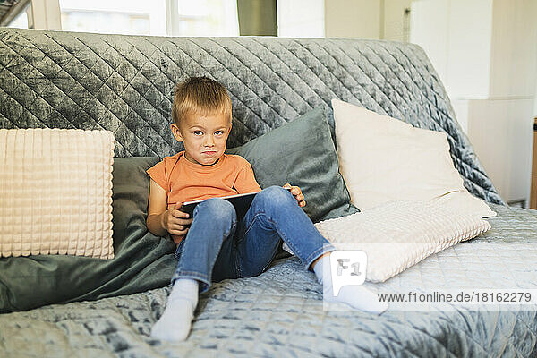 Cute boy with tablet PC sitting on sofa at home