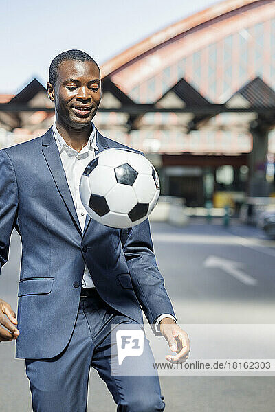 Happy businessman playing with soccer ball on sunny day