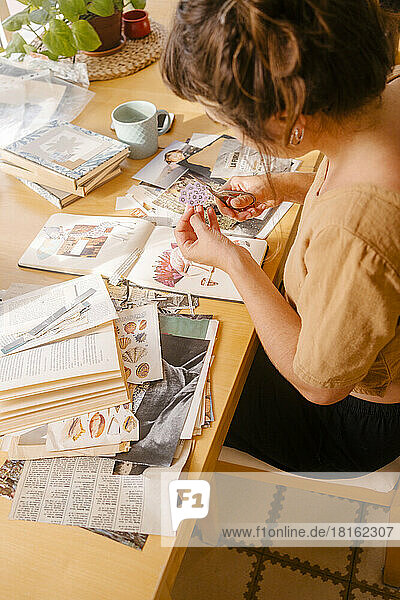 Graphic designer cutting paper clipping sitting at desk in home