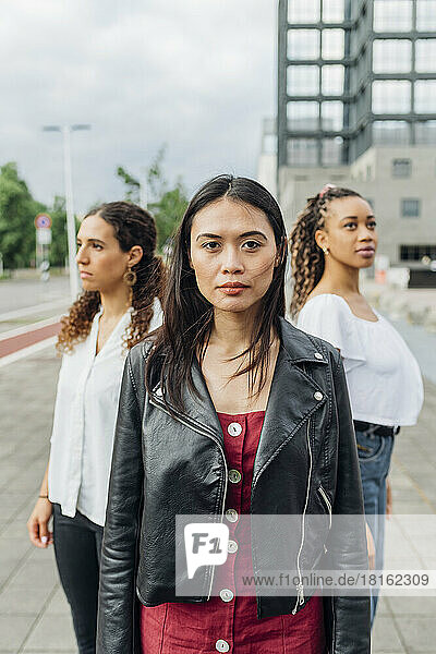 Confident woman with friends in background on footpath