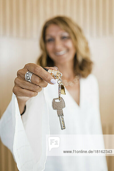 Mature businesswoman giving keys standing in front of wall