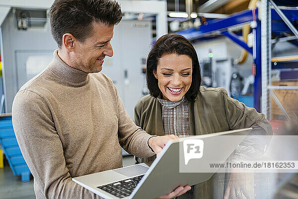 Smiling businessman showing laptop to businesswoman in industry