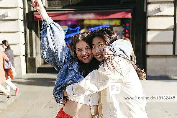 Happy lesbian women embracing each other at street on sunny day