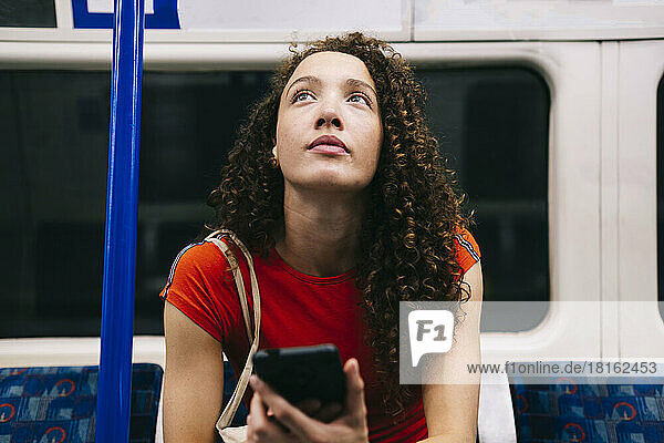 Contemplative young woman with smart phone sitting in subway train