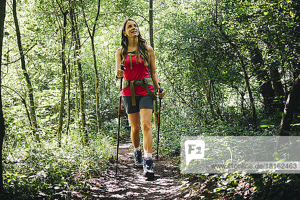 Woman exploring forest walking with hiking poles on trail