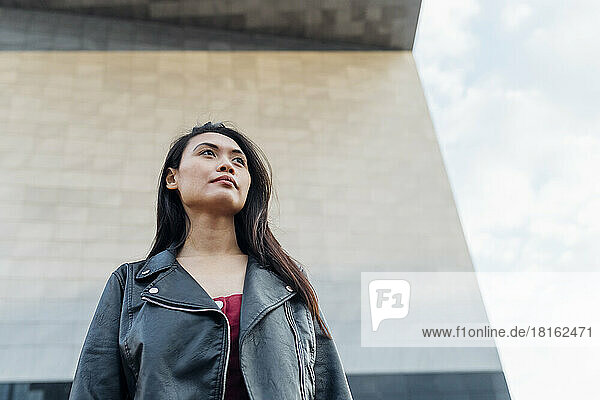 Thoughtful woman wearing leather jacket in front of wall