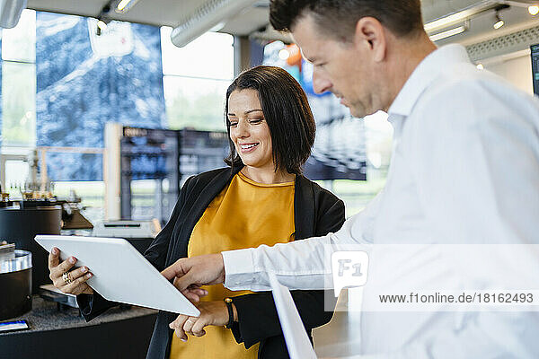 Smiling businesswoman sharing tablet PC with colleague in industry