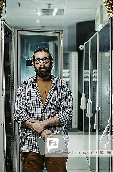 Computer programmer with beard holding tablet PC in server room