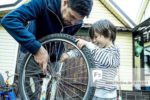 Son helping father repairing bicycle wheel outside house