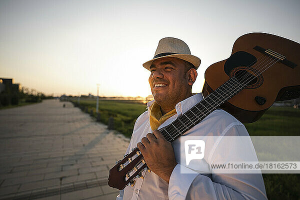 Smiling street musician wearing hat carrying guitar on shoulder