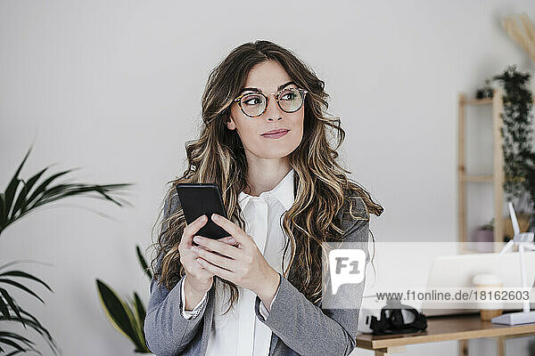 Thoughtful businesswoman using mobile phone in office