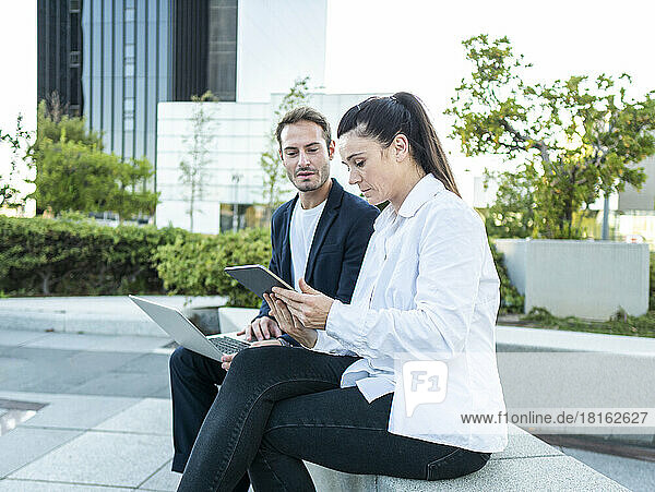 Businesswoman sharing tablet PC with businessman sitting at office park