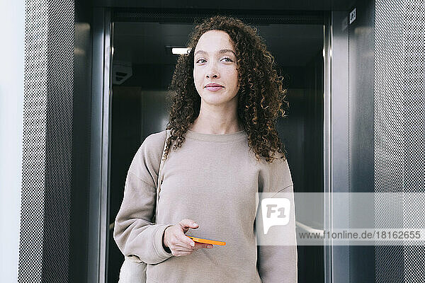 Smiling woman holding smart phone exiting from elevator