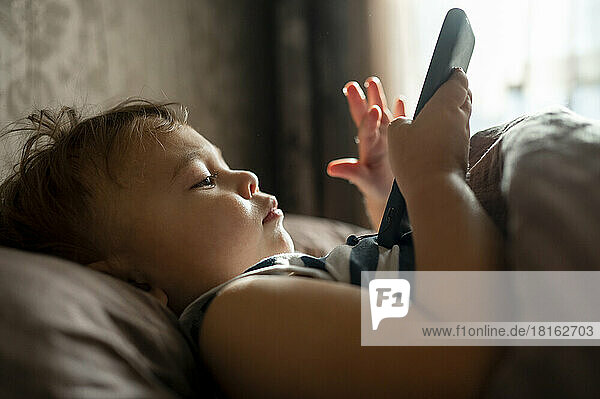 Baby Junge benutzt Handy im Bett liegend