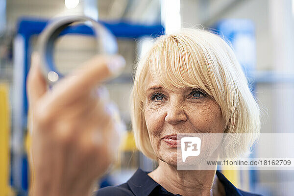 Smiling senior businesswoman analyzing machine part in industry