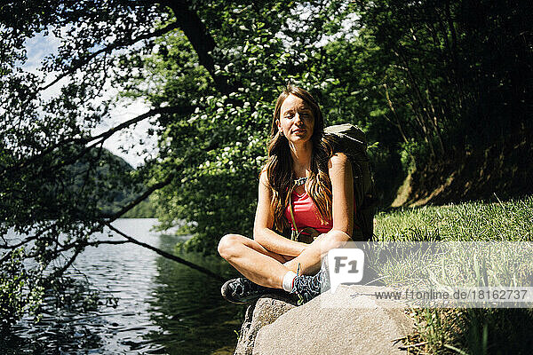 Woman with eyes closed sitting cross-legged near Lake Levico