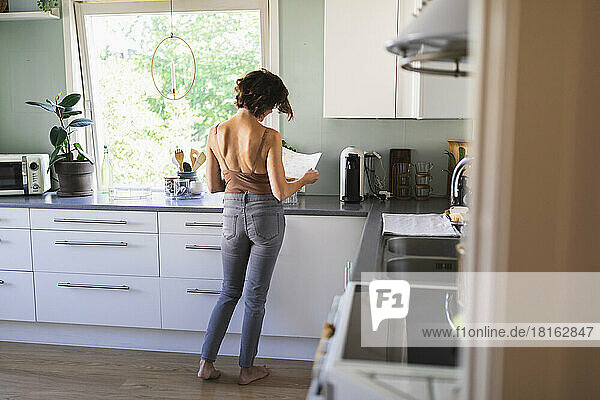 Woman looking at paper standing in kitchen