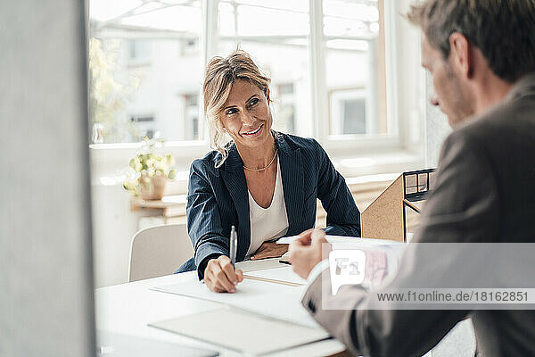 Businesswoman discussing with client reading agreement at office