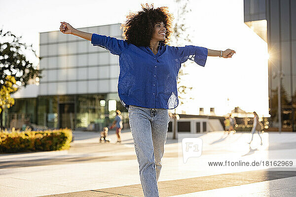 Happy woman with arms outstretched walking on footpath