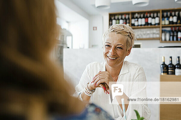 Happy blond woman sitting with friend in restaurant