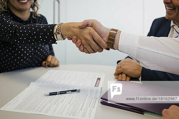 Reife Geschäftsfrau schüttelt einem Kollegen am Schreibtisch im Büro die Hand