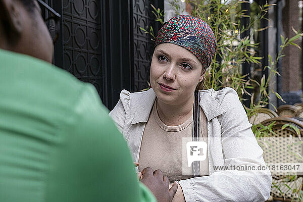 Young woman wearing bandana talking with friend at sidewalk cafe