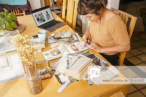 Graphic designer sticking paper clippings in book working at home