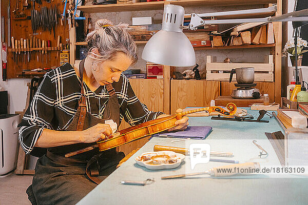 Gitarrenbauer poliert und repariert Geige am Schreibtisch in der Werkstatt