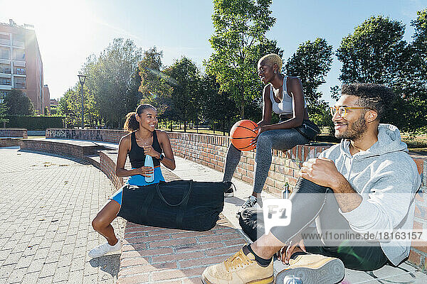 Smiling multiracial friends after basketball practice sitting on wall