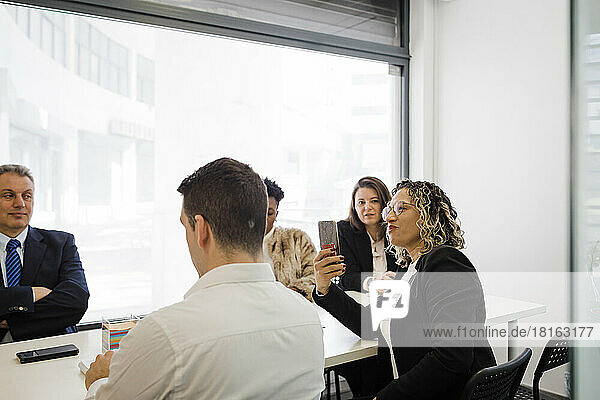 Smiling businesswoman photographing through smart phone in meeting at office