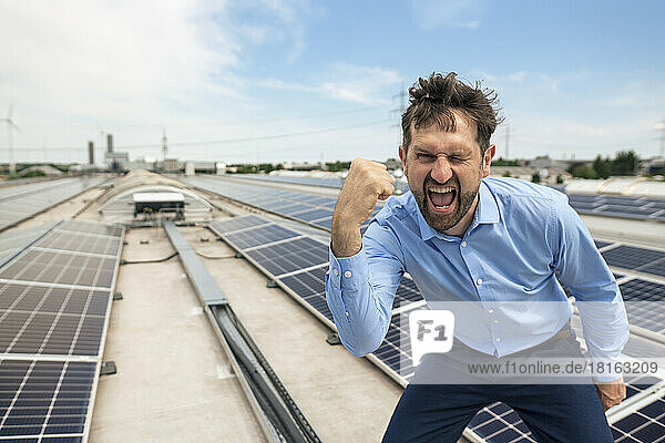 Businessman with mouth open gesturing fist in front of solar panels