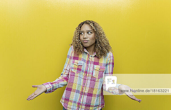 Verwirrte blonde Frau im karierten Hemd vor gelbem Hintergrund