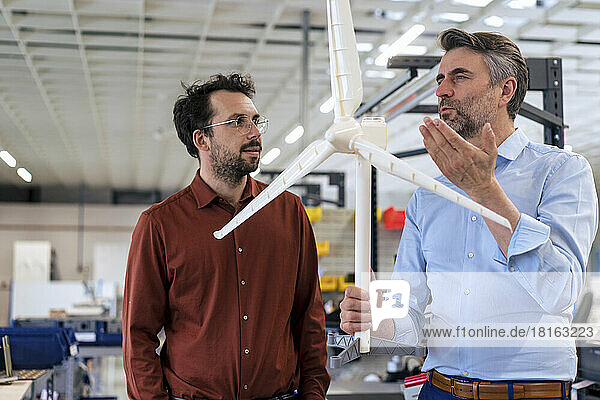 Mature businessman holding wind turbine discussing with colleague at warehouse